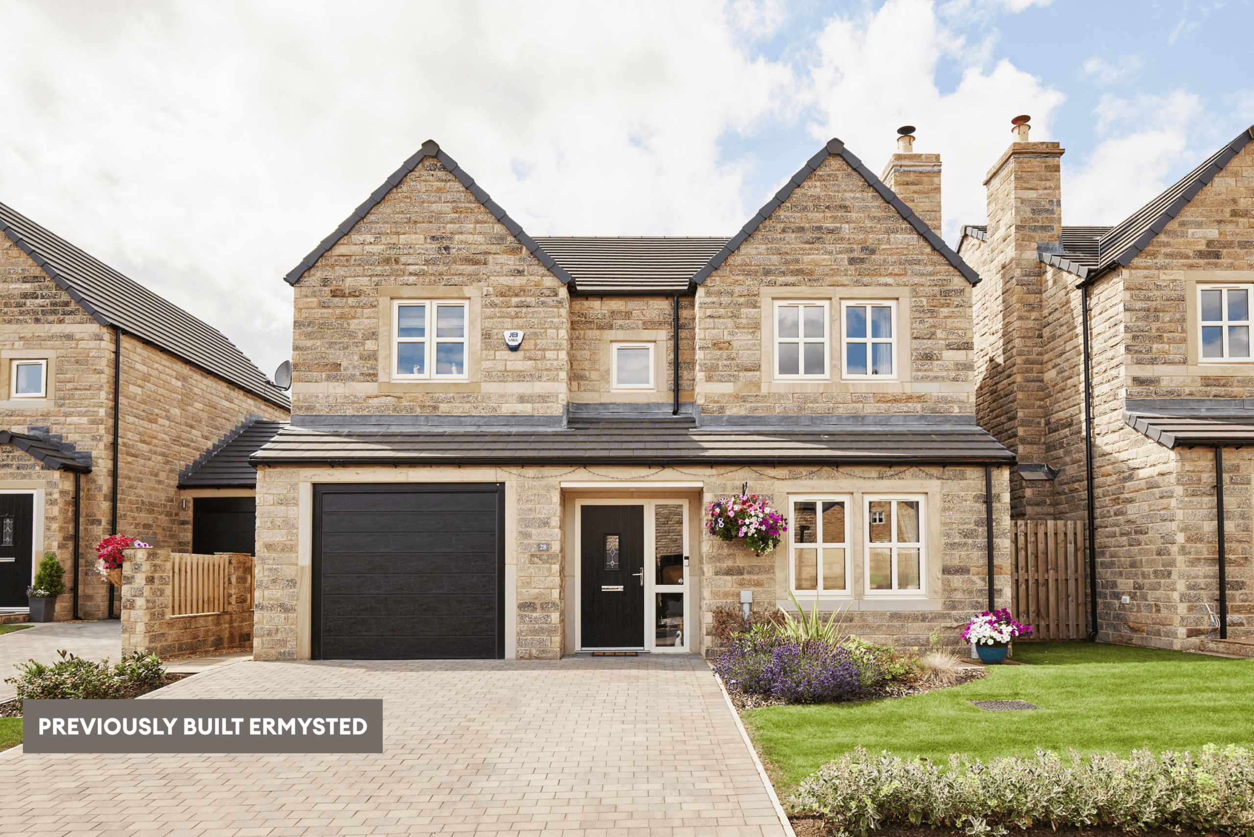 Previously built Ermysted home in natural stone, with an integral garage, black front door, paved driveway and landscaped front garden.