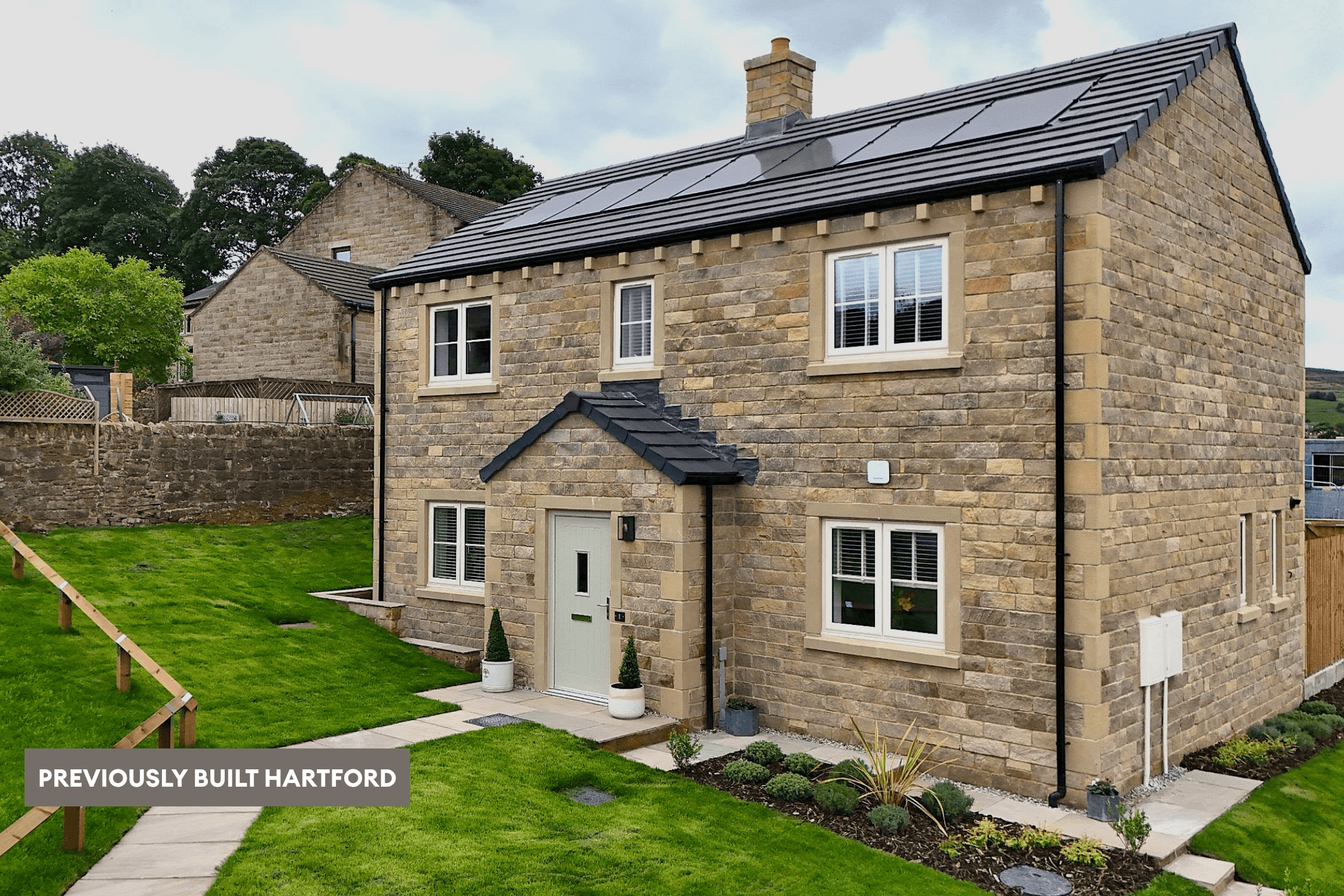 Previously built Hartford home in natural stone, featuring roof-mounted solar panels, a pale front door and landscaped lawn and garden.