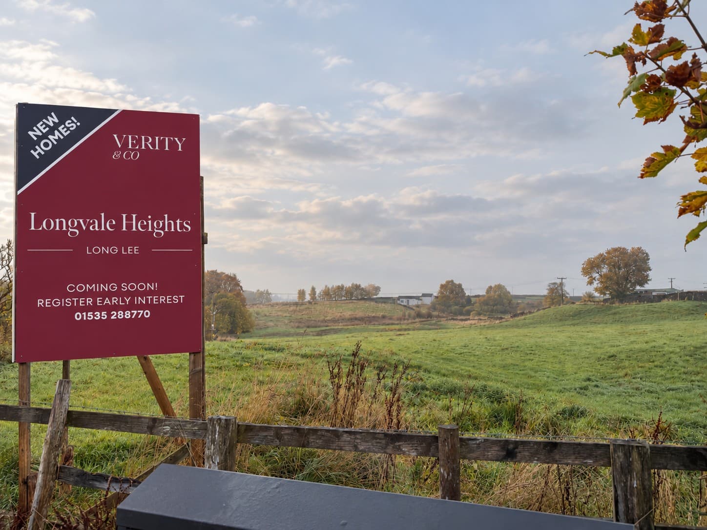 Longvale Heights development sign by Verity & Co Homes, positioned beside open green countryside in Long Lee, with mature trees and autumnal scenery beyond.